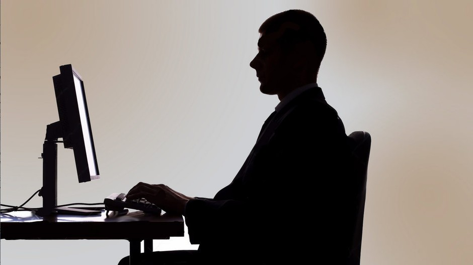 Muž sedí za počítačom v tieni